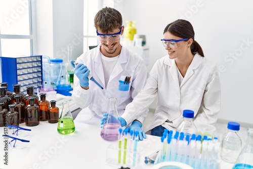 Man and woman partners wearing scientist uniform holding test tube and pipette at laboratory