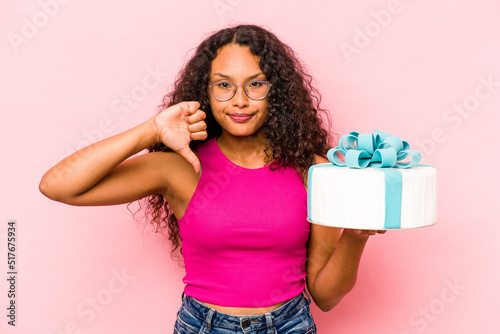Young caucasian woman holding a cake isolated on pink background showing a dislike gesture, thumbs down. Disagreement concept.