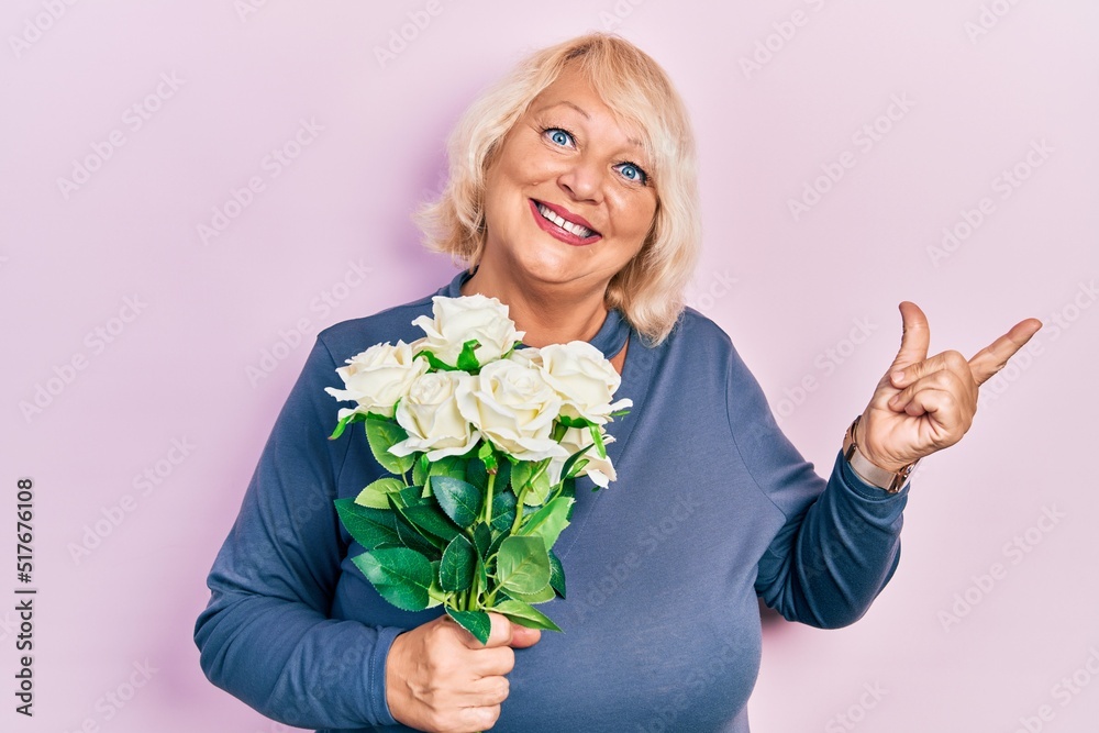 Middle age blonde woman holding flowers smiling happy pointing with hand and finger to the side Middle age blonde woman holding flowers smiling happy pointing with hand and finger to the side