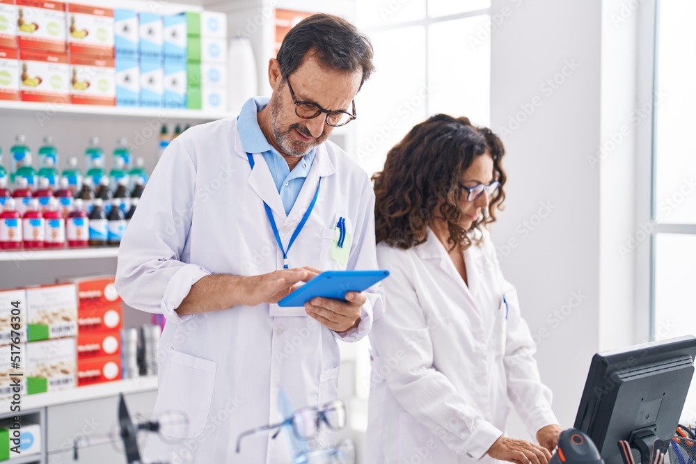 Man and woman pharmacists using touchpad and computer at pharmacy Man and woman pharmacists using touchpad and computer at pharmacy