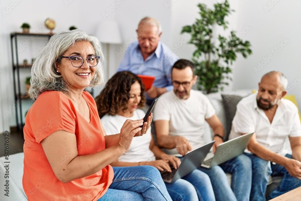 Group of middle age friends using laptop and smartphone sitting on the sofa at home.