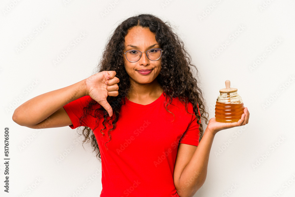 Young hispanic woman holding honey jar isolated on white background showing a dislike gesture, thumbs down. Disagreement concept. Young hispanic woman holding honey jar isolated on white background showing a dislike gesture, thumbs down. Disagreement concept.