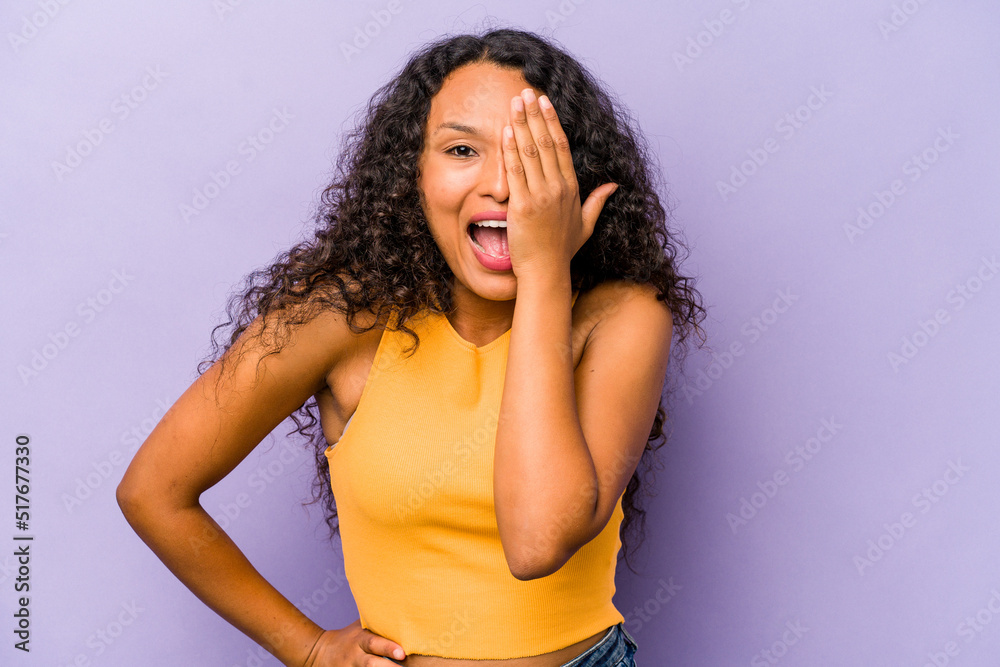 Young hispanic woman isolated on purple background having fun covering half of face with palm. Young hispanic woman isolated on purple background having fun covering half of face with palm.