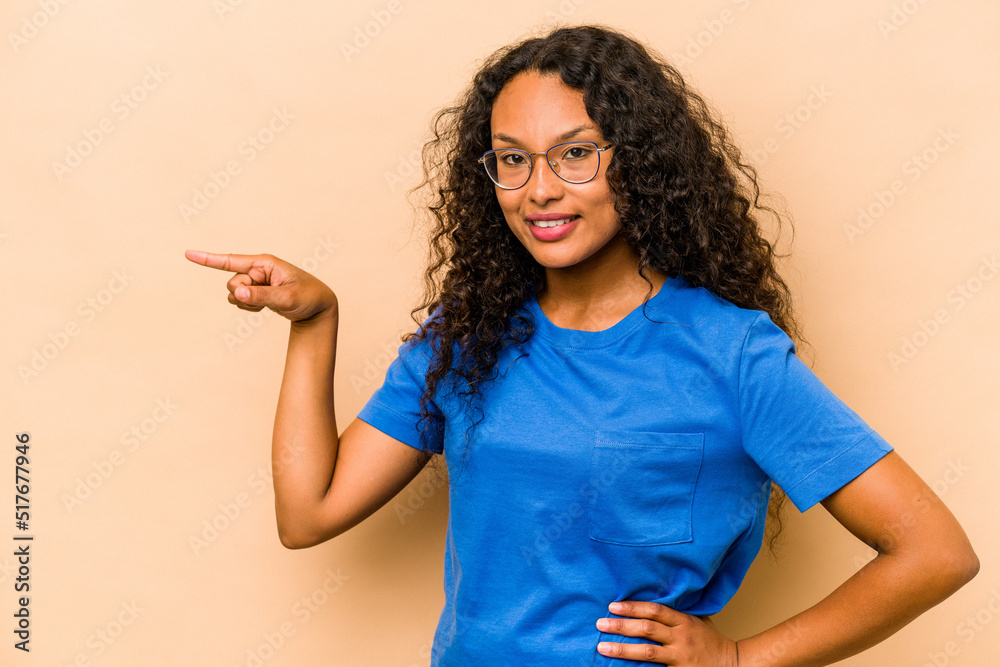Young hispanic woman isolated on beige background smiling cheerfully pointing with forefinger away.