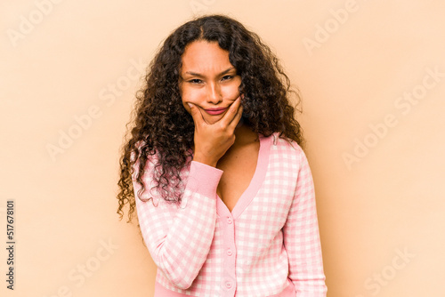 Young hispanic woman isolated on beige background doubting between two options.