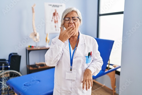 Obraz na plátne Middle age woman with grey hair working at pain recovery clinic bored yawning tired covering mouth with hand