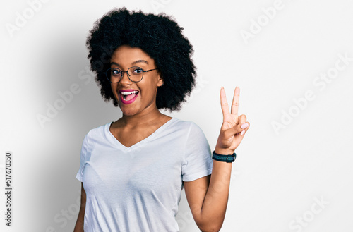 Young african american woman wearing casual white t shirt smiling with happy face winking at the camera doing victory sign with fingers. number two.
