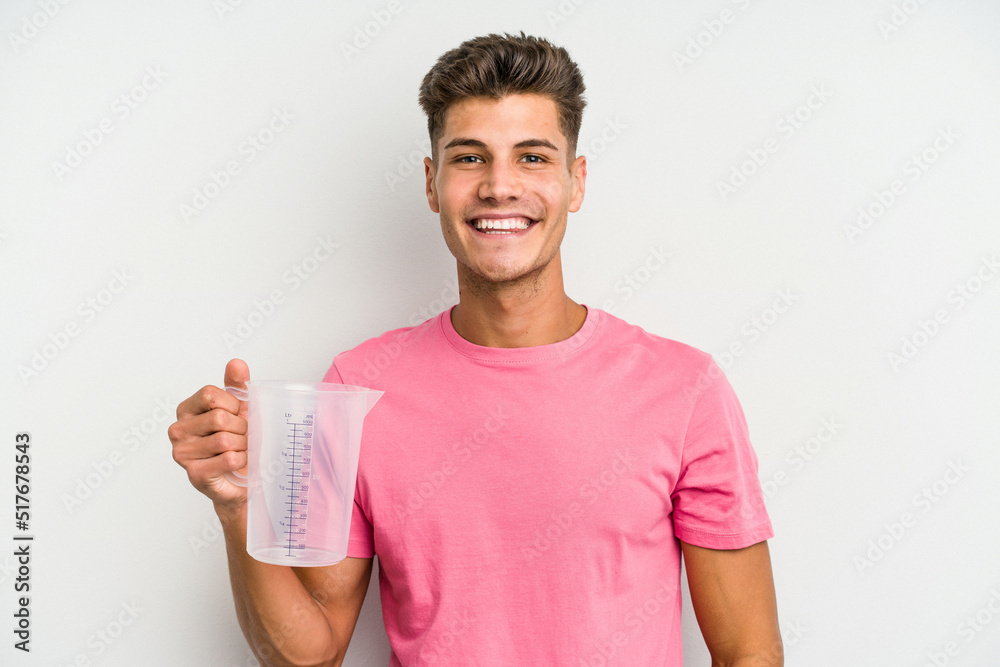 Young caucasian man holding measuring jug isolated on white background happy, smiling and cheerful. Young caucasian man holding measuring jug isolated on white background happy, smiling and cheerful.