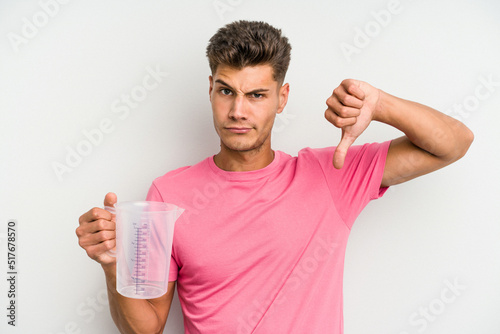 Young caucasian man holding measuring jug isolated on white background showing a dislike gesture, thumbs down. Disagreement concept.