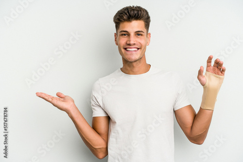 Young caucasian man hand sling isolated on white background showing a copy space on a palm and holding another hand on waist.