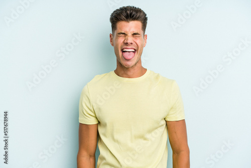 Young caucasian man isolated on blue background funny and friendly sticking out tongue.