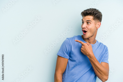 Young caucasian man isolated on blue background points with thumb finger away, laughing and carefree.