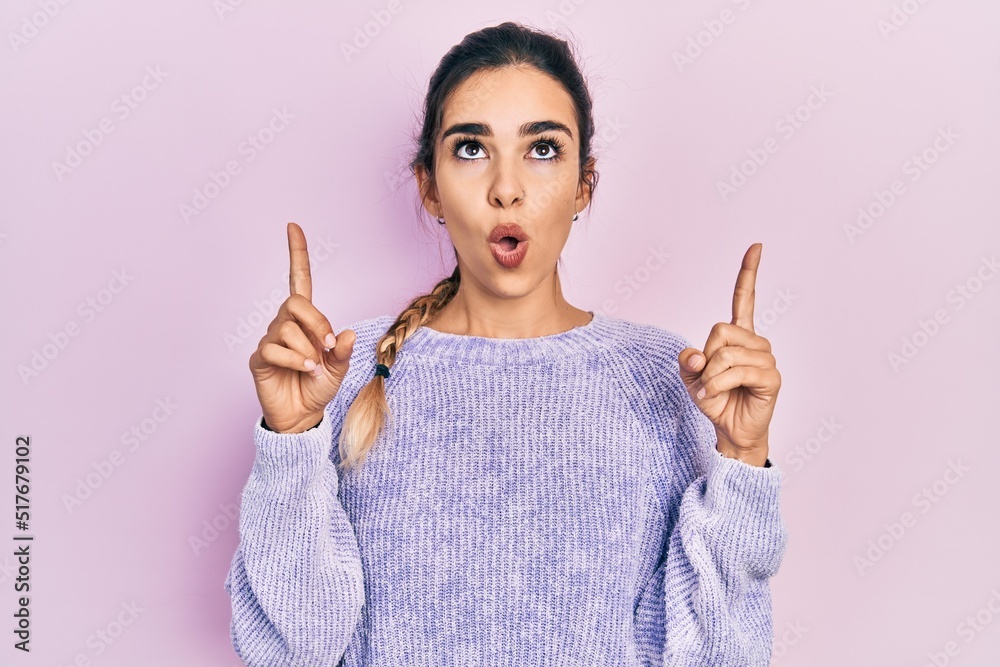 Young hispanic girl wearing casual clothes amazed and surprised looking up and pointing with fingers and raised arms. Young hispanic girl wearing casual clothes amazed and surprised looking up and pointing with fingers and raised arms.
