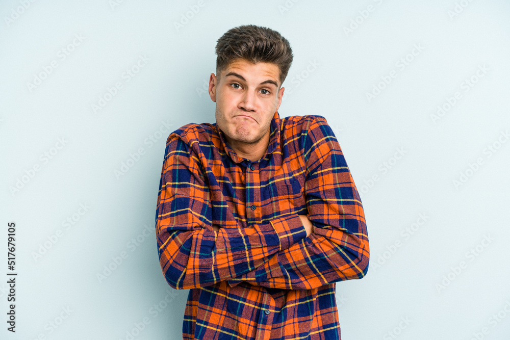 Young caucasian man isolated on blue background shrugs shoulders and open eyes confused. Young caucasian man isolated on blue background shrugs shoulders and open eyes confused.