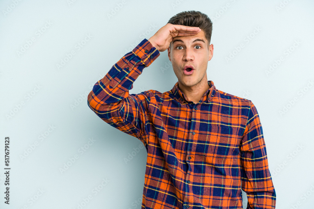 Young caucasian man isolated on blue background looking far away keeping hand on forehead.