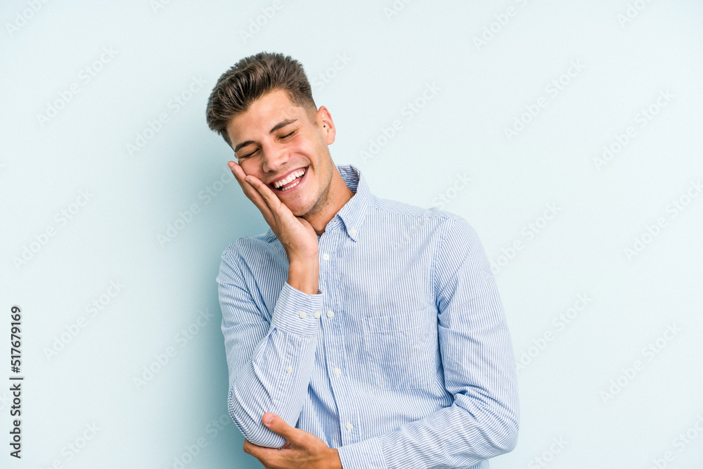 Young caucasian man isolated on blue background laughs happily and has fun keeping hands on stomach. Young caucasian man isolated on blue background laughs happily and has fun keeping hands on stomach.