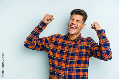 Young caucasian man isolated on blue background raising fist after a victory, winner concept. © Asier