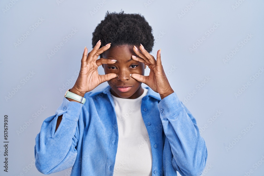 African american woman standing over blue background trying to open eyes with fingers, sleepy and tired for morning fatigue African american woman standing over blue background trying to open eyes with fingers, sleepy and tired for morning fatigue