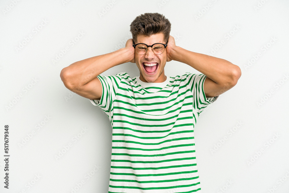 Young caucasian man isolated on white background covering ears with hands trying not to hear too loud sound. Young caucasian man isolated on white background covering ears with hands trying not to hear too loud sound.