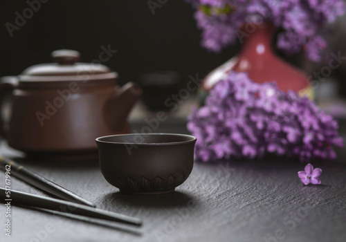 Brown ceramic asian teapot , tea cups and chopsticks on background of purple flowers. Japanese food concept