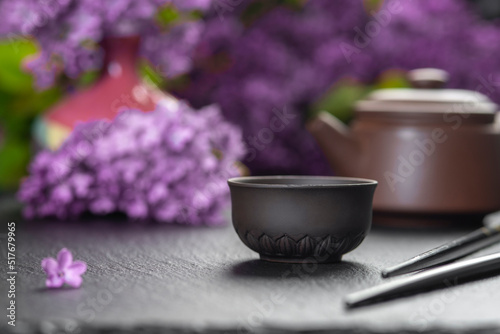 Brown ceramic asian teapot , tea cups and chopsticks on background of purple flowers. Japanese food concept