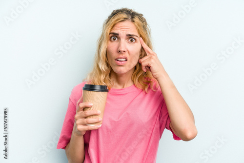 Young caucasian woman holding a take away coffee isolated on blue background showing a disappointment gesture with forefinger.