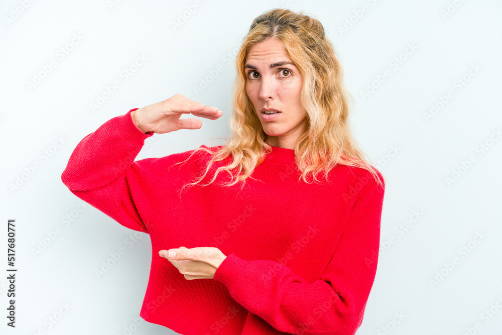 Young caucasian woman isolated on blue background holding something with both hands, product presentation. Young caucasian woman isolated on blue background holding something with both hands, product presentation.