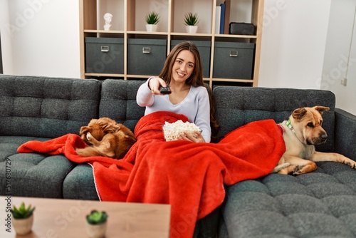 Wallpaper Mural Young hispanic woman watching movie sitting on sofa with dogs at home Torontodigital.ca