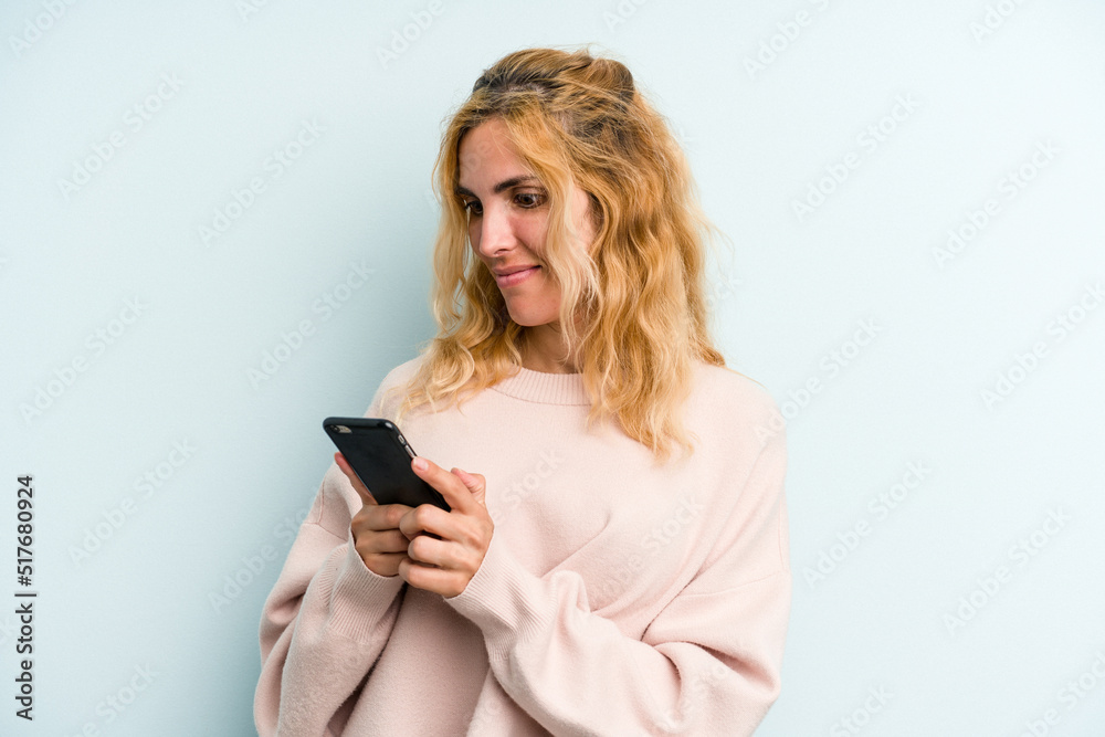 Young caucasian woman holding mobile phone isolated on blue background Young caucasian woman holding mobile phone isolated on blue background