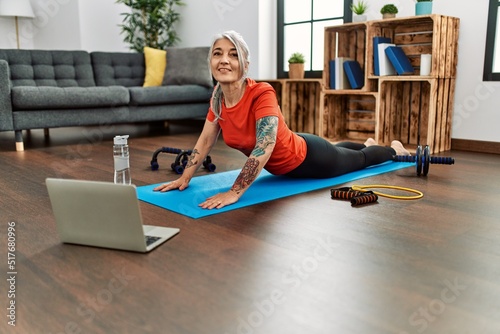 Middle age grey-haired woman smiling confident having online stretching class at home