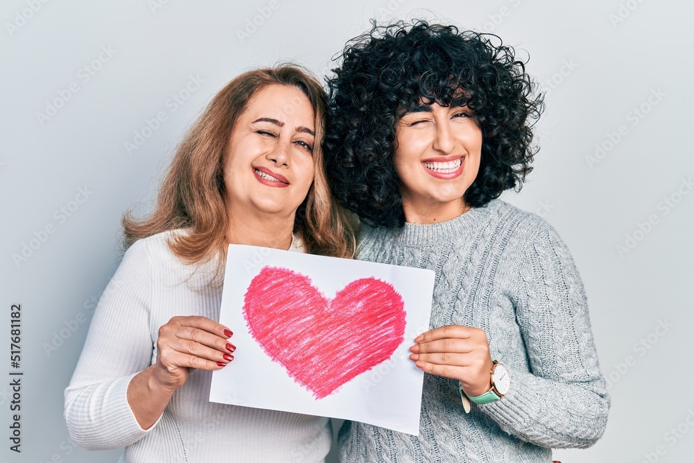 Middle east mother and daughter holding paper with heart draw winking looking at the camera with sexy expression, cheerful and happy face. Middle east mother and daughter holding paper with heart draw winking looking at the camera with sexy expression, cheerful and happy face.