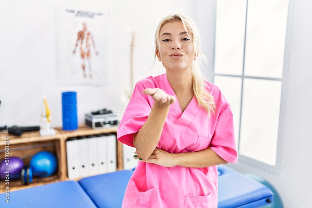 Young caucasian woman working at pain recovery clinic looking at the camera blowing a kiss with hand on air being lovely and sexy. love expression.