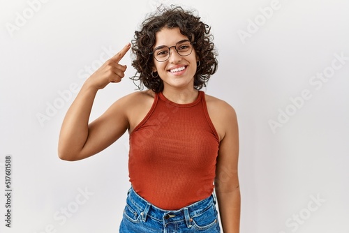 Young hispanic woman wearing glasses standing over isolated background smiling pointing to head with one finger, great idea or thought, good memory