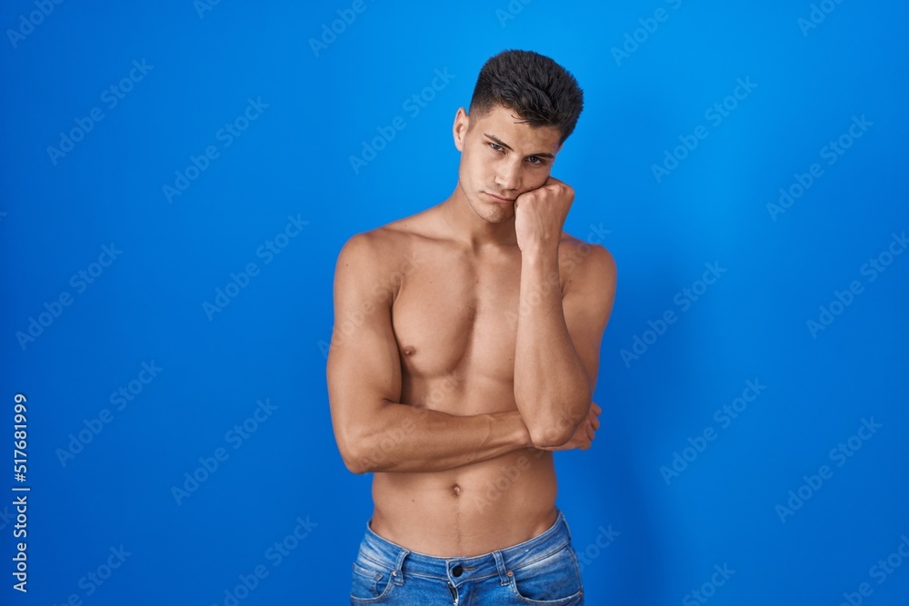 Obraz premium Young hispanic man standing shirtless over blue background thinking looking tired and bored with depression problems with crossed arms.