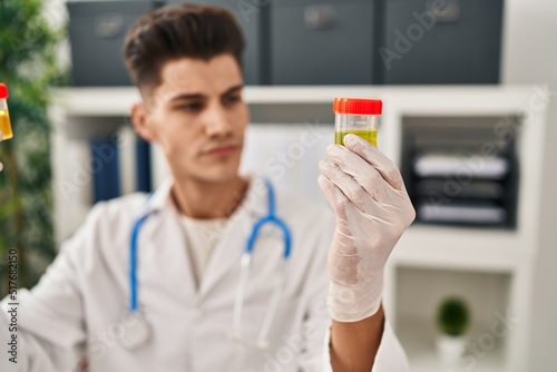 Young hispanic man wearing doctor uniform analysing urine test tubes at clinic