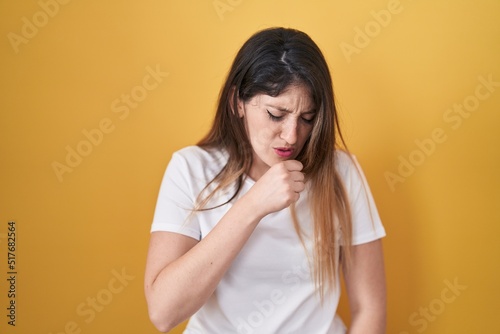 Young brunette woman standing over yellow background feeling unwell and coughing as symptom for cold or bronchitis. health care concept.