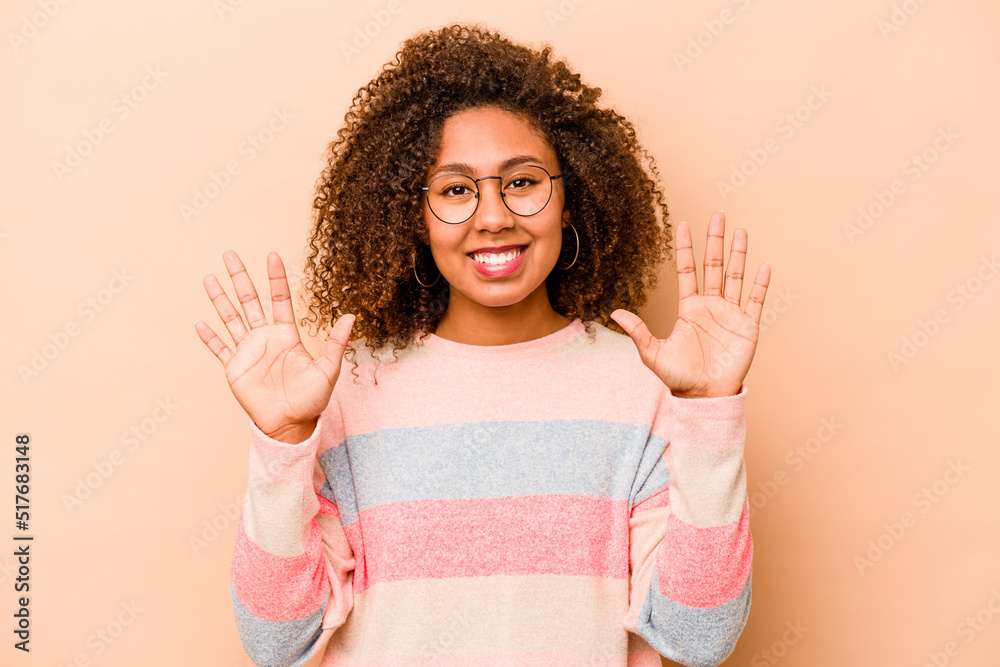 Young African American woman isolated on beige background showing number ten with hands. Young African American woman isolated on beige background showing number ten with hands.