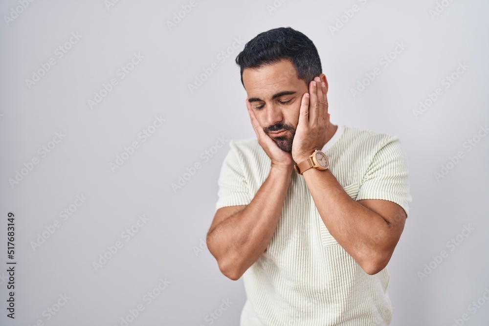 Hispanic man with beard standing over isolated background tired hands covering face, depression and sadness, upset and irritated for problem