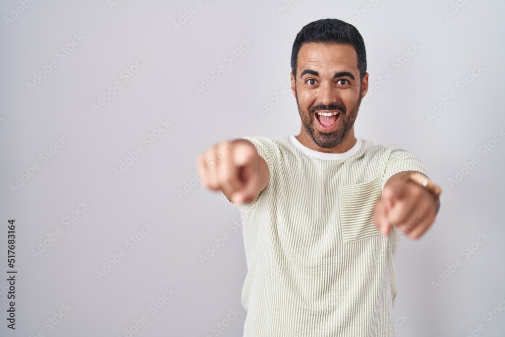 Fototapeta premium Hispanic man with beard standing over isolated background pointing to you and the camera with fingers, smiling positive and cheerful