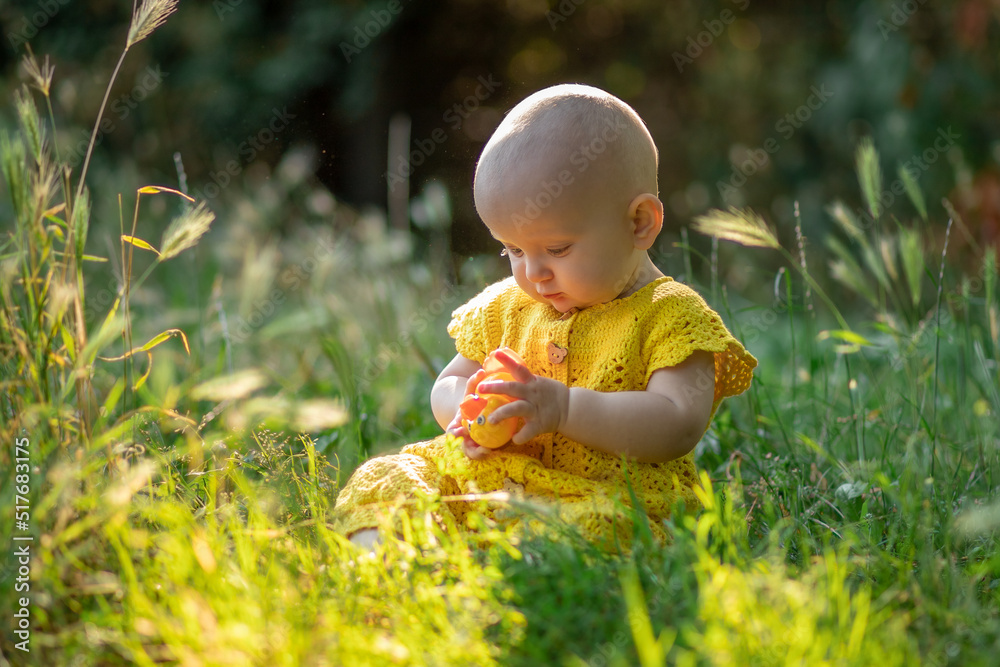 little cute happy baby girl sitting on the green grass on a sunny summer day dressed in knitted cotton yellow jumpsuit. little cute happy baby girl sitting on the green grass on a sunny summer day dressed in knitted cotton yellow jumpsuit.