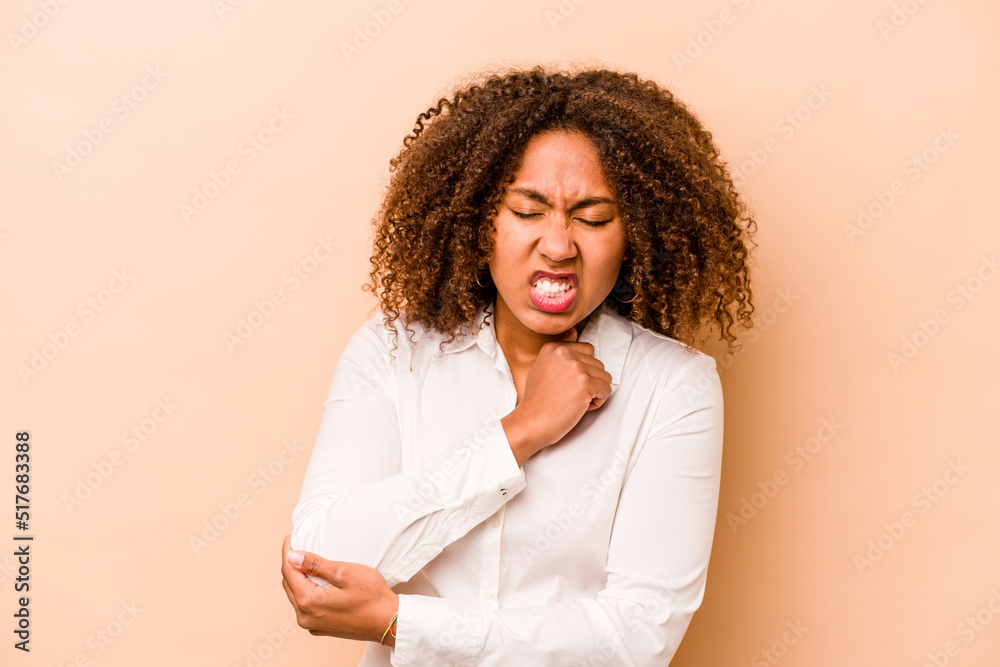 Young African American woman isolated on beige background massaging elbow, suffering after a bad movement. Young African American woman isolated on beige background massaging elbow, suffering after a bad movement.