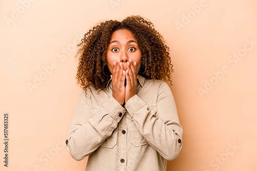 Young African American woman isolated on beige background shocked covering mouth with hands.