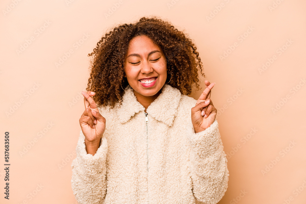 Young African American woman isolated on beige background crossing fingers for having luck Young African American woman isolated on beige background crossing fingers for having luck
