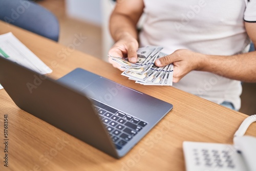 Young hispanic man business worker counting dollars working at office