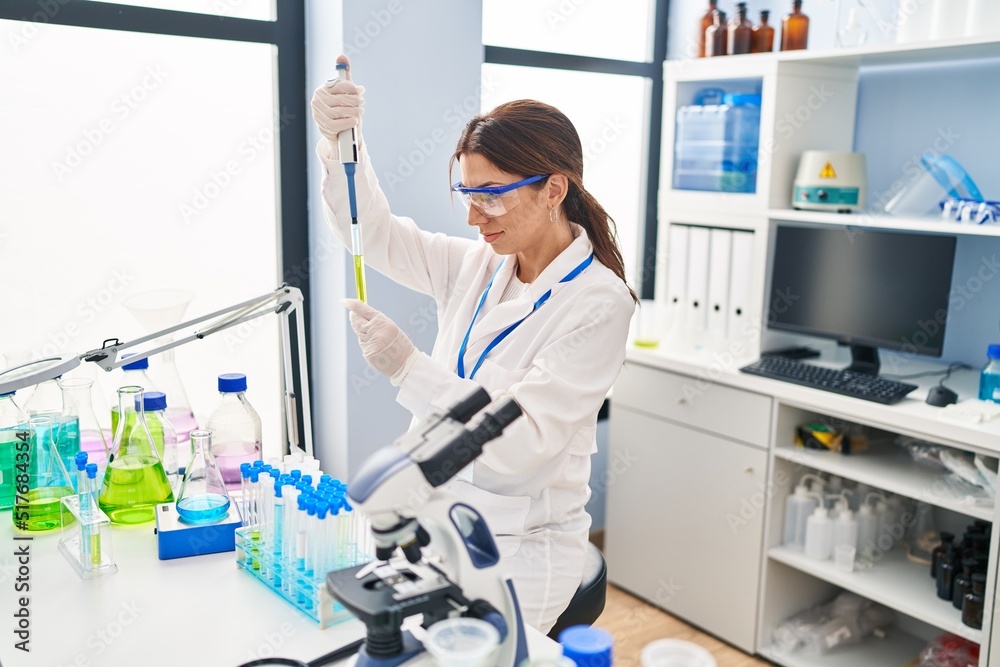 Young hispanic woman wearing scientist uniform using pipette at laboratory Young hispanic woman wearing scientist uniform using pipette at laboratory