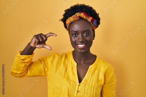 African young woman wearing african turban smiling and confident gesturing with hand doing small size sign with fingers looking and the camera. measure concept.