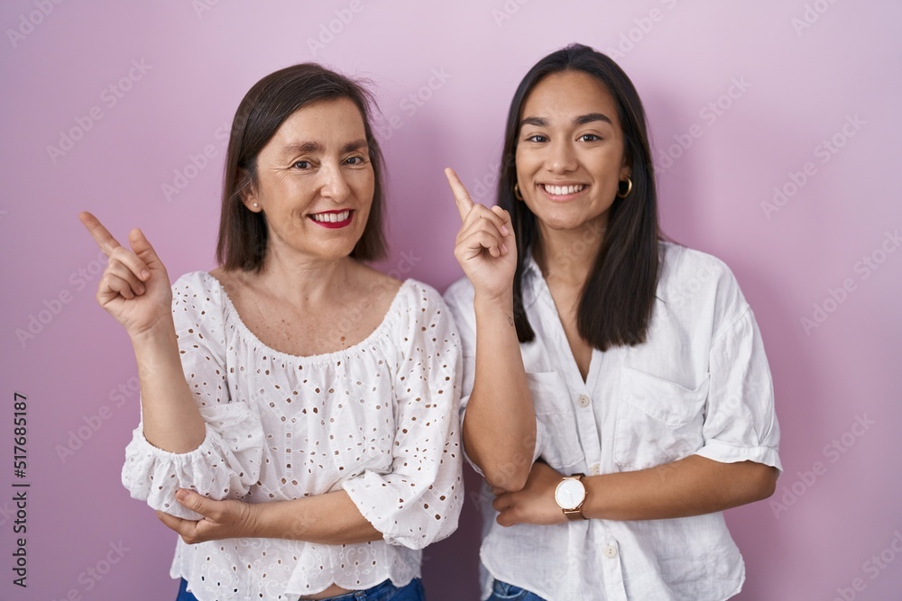 Hispanic mother and daughter together with a big smile on face, pointing with hand finger to the side looking at the camera. Hispanic mother and daughter together with a big smile on face, pointing with hand finger to the side looking at the camera.