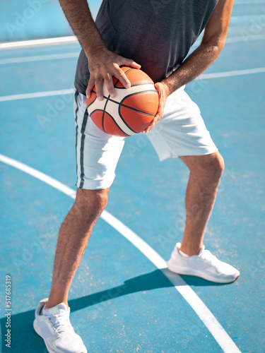 Close-up image of hands of adult basketball player holding a sport ball at waist level ready to pass it