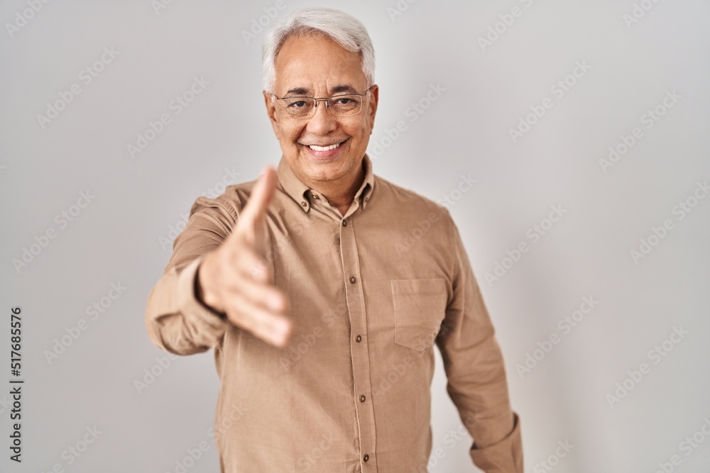 Hispanic senior man wearing glasses smiling friendly offering handshake as greeting and welcoming. successful business. Hispanic senior man wearing glasses smiling friendly offering handshake as greeting and welcoming. successful business.