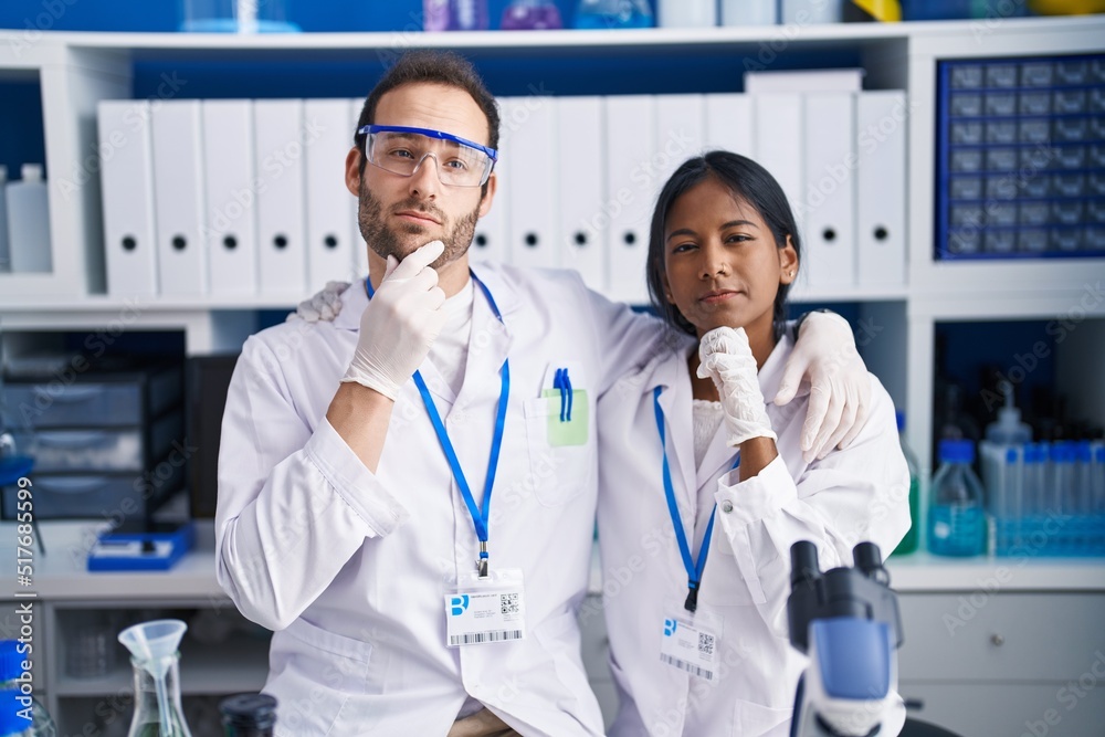 Interracial couple working at scientist laboratory serious face thinking about question with hand on chin, thoughtful about confusing idea Interracial couple working at scientist laboratory serious face thinking about question with hand on chin, thoughtful about confusing idea